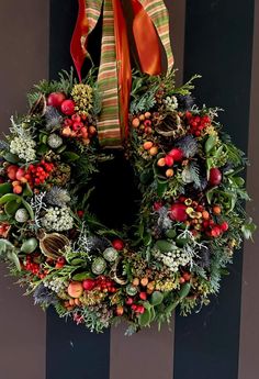 a wreath hanging on the front door with red and green decorations, greenery and berries