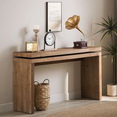 a wooden table with a clock and other items on it next to a plant in a room