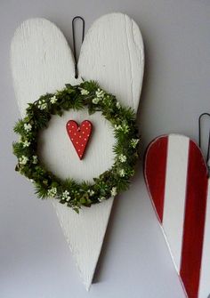 two wooden heart shaped ornaments hanging on the wall next to each other, one with a wreath