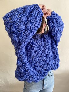 a woman wearing a blue knitted sweater covering her face with one hand and holding the other over her head