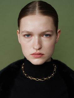 a model with blue eyes wearing a black turtle neck sweater and gold chain choker