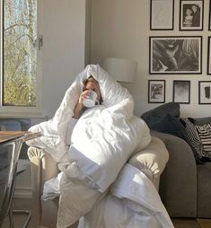 a woman wrapped up in a blanket and holding a coffee cup while sitting on a couch