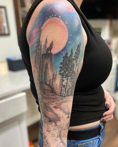 a woman's arm with a painting on it that has trees in the background