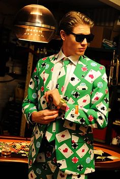 a man in a green suit and sunglasses standing next to a table with poker cards on it