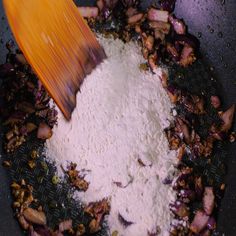 a wooden spatula scooping food out of a pan filled with white powder and vegetables