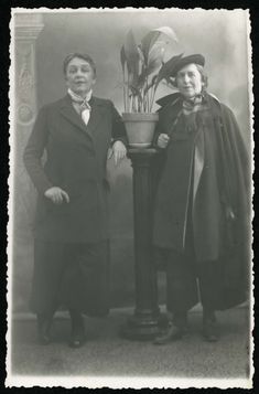 an old black and white photo of two people standing next to each other in front of a potted plant