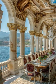 an ornate dining room with columns and chandeliers on the ceiling, overlooking water