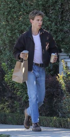 a man is walking down the street carrying shopping bags and holding a coffee in his hand