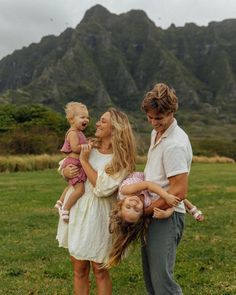 a man, woman and child are standing in the grass with mountains in the background