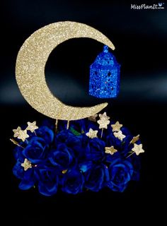 a blue and gold centerpiece with a house on the moon next to it, surrounded by roses