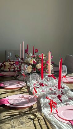 the table is set with pink and white plates, silverware, candles and flowers