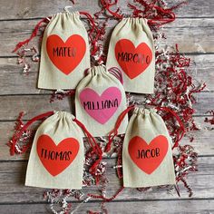 four small bags with red and pink hearts on them sitting next to shredded tinsel