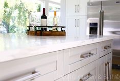 two bottles of wine are sitting on the counter in this white kitchen with stainless steel appliances