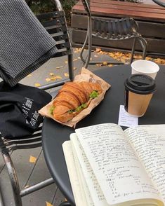 an open book sitting on top of a table next to a cup of coffee and a sandwich