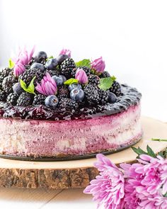 a blueberry cheesecake with fresh blackberries and purple flowers on a wooden board