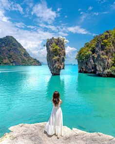 a woman sitting on the edge of a cliff looking out at an island in the ocean