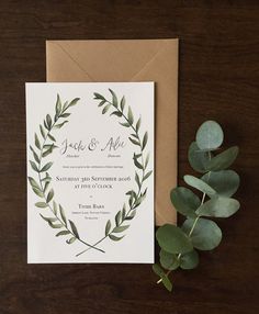 a wedding card with greenery on it next to a leafy branch and brown envelope