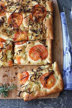 a square pizza with tomatoes and herbs on a cutting board