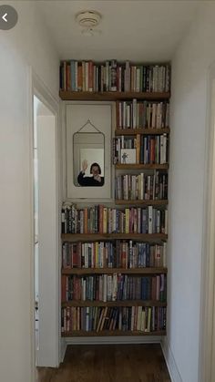 a book shelf filled with lots of books next to a mirror on the wall above it