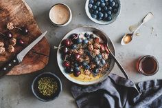 a bowl filled with cereal and berries next to two bowls of fruit on a cutting board