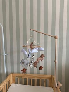 a baby crib with an animal mobile hanging from it's side, in front of striped wallpaper