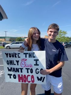 two people standing in a parking lot holding a sign that says you're the only chick i want to go to hoco