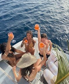 four people sitting on a boat with drinks in their hands and one person holding up an orange