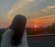 a woman standing on top of a roof watching the sun go down