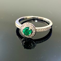 an emerald and diamond ring sitting on top of a black surface with reflection in it