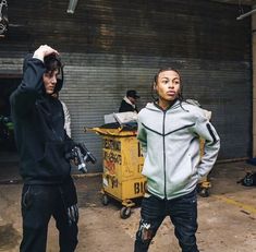 two young men standing next to each other in front of a garage door, one with his hand on his head