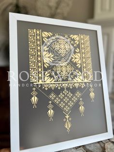 a black and gold art print with an intricate design on the front, in a white frame