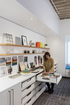 a woman sitting at a desk in an office with lots of papers on the shelves