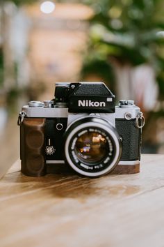 a nikon camera sitting on top of a wooden table next to a potted plant