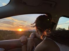 a woman is sitting in the back seat of a car as the sun sets