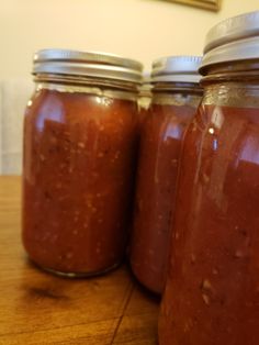 three jars filled with red sauce sitting on top of a wooden table