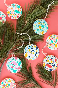 some paper ornaments are hanging from a pine branch on a pink background with green branches