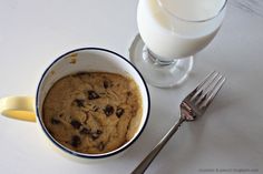 a bowl of chocolate chip cookies next to a glass of milk and a fork on a table