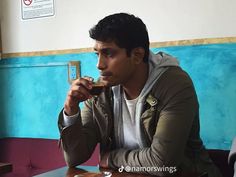 a man sitting at a table eating food with a cell phone in his hand and looking off to the side