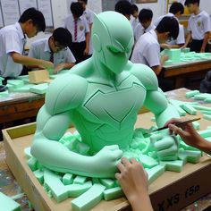 a group of people working on a green statue in a room filled with desks