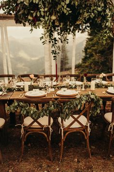 the table is set with white plates and place settings, greenery on each plate