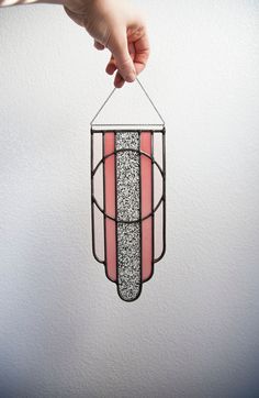 a hand holding a pink and black stained glass hanging light fixture with glittery stripes