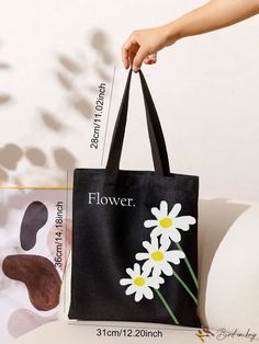 a person holding a black bag with white daisies on it and the words flower printed on it