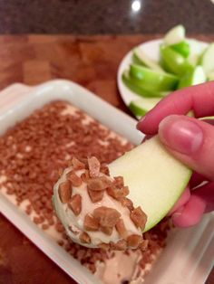 a person is holding an apple slice over a dessert in a white dish on a wooden table