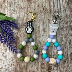 two key chains with charms on them sitting next to some plants and flowers, one has a hand print