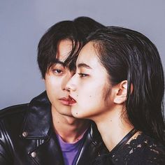 two people are posing for the camera with their heads close to each other, one is wearing a leather jacket and the other has long black hair