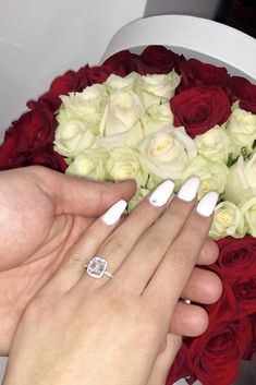 two hands holding a bouquet of white and red roses with a diamond ring on it