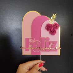 a hand holding up a pink and gold birthday card with flowers on it that says feliz