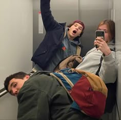 three people on the subway taking pictures with their cell phones while one person is laying down