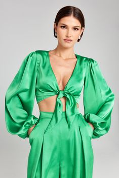 Vicky Green Tie Top Women's Clothing > Tops.     DESCRIPTION &  FEATURES    VICKY  is a voluminous, long-sleeved tie top crafted from green satin fabric, featuring a plunging v-neckline, blouson sleeves, elasticated cuffs, self-ties to be worn in a knot at the front, and finished with a  green  satin lining.         Pair it with the    DANIELLA Green Trousers  to com  plete the look.      - Green satin fabric    - Low plunge v-neckline   - Self-tie to the front   - Gathering blouson sleeves   - Green Satin Fabric, Nadine Merabi, Pajama Suit, Green Trousers, Top Crafts, Green Tie, Green Satin, Tie Top, Satin Fabric