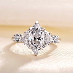 a three stone diamond ring sitting on top of a white cloth covered table with a light colored background